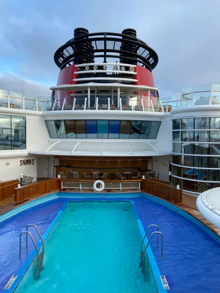 An early morning view of the pool within Quiet Cove with the Signals Bar overlooking the pool area. An early morning view of the quiet cove pool area beneath the ship funnels from our Disney cruise for adults trip.