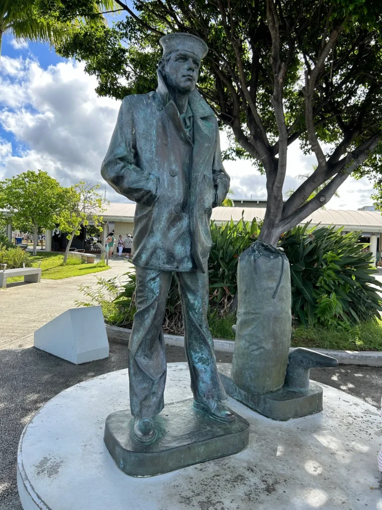 Along the pathway at Pearl Harbor is The Lone Sailor. The statue is dedicated to all that have served in the US Navy. The bronze Lone Sailor statue standing along the harbor shoreline path at the Pearl Harbor Memorial Hawaii.