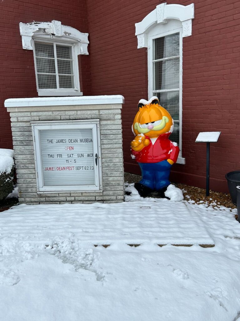 The entrance to the James Dean Museum, where you are welcomed by another Indiana legend, Garfield striking that famous James Dean pose. A snowy winter view of the James Dean Museum entrance sign alongside a large statue of Garfield the cat wearing a red jacket in Indiana.