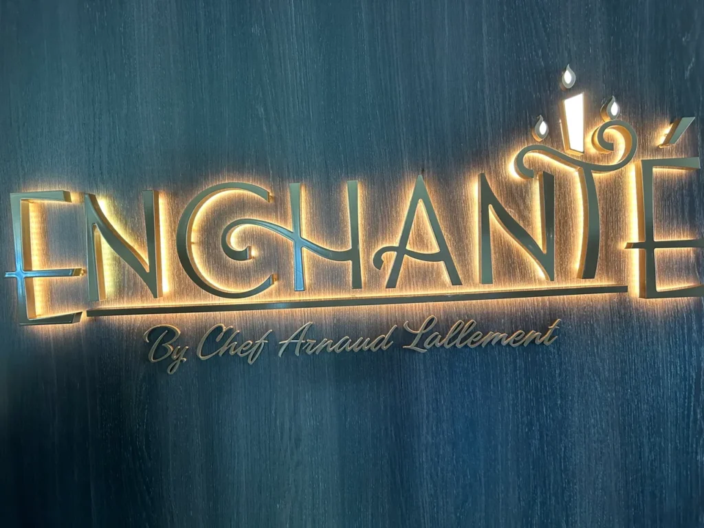 The elegant, glowing gold Enchanté by Chef Arnaud Lallement entrance sign featured in our Disney Wish dining guide.