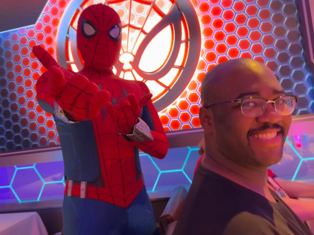 Spider Man posing for a photo with a smiling male guest during the Worlds of Marvel character dining experience on the Disney Wish.