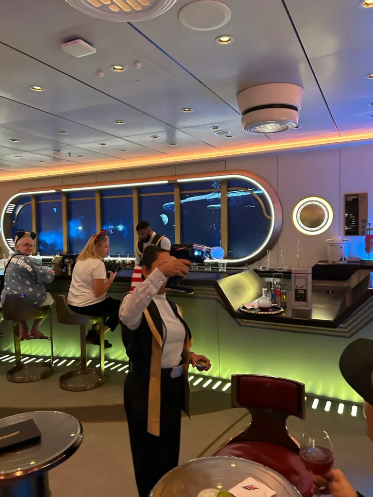 A crew member using a flavor blaster gun to create a smoke bubble on a cocktail inside the Star Wars Hyperspace Lounge, featured in our Disney Wish dining guide.