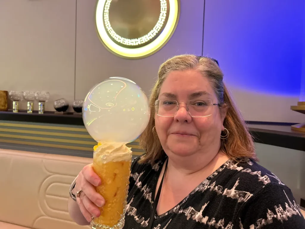A guest smiling with a glowing specialty drink inside the Star Wars Hyperspace Lounge from our Disney Wish dining guide.