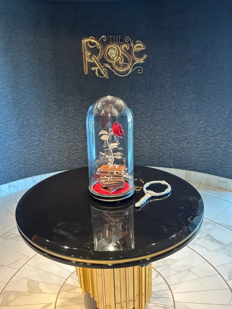 The iconic enchanted rose under a glass dome greeting guests at the entrance of The Rose lounge from our Disney Wish dining guide.