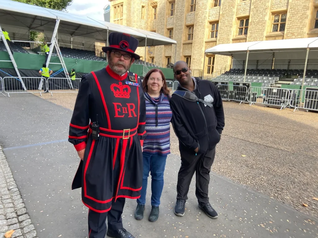 The official duties of the Yeoman Warders are to project the Tower of London and its contents which includes the Crown Jewels. Unofficially they are the guides for the thousands of tourists that visit each year. They are also very open to a memorable photo too. A friendly Yeoman Warder Beefeater posing for a photo with two tourists inside the courtyard at the Tower of London planning guide site.