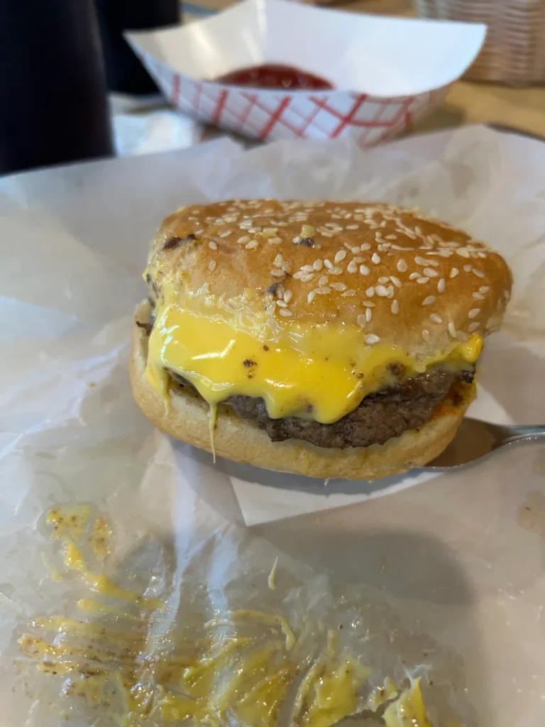 The legend - a cheeseburger from Redamak's, dripping with Velvetta which makes this sandwich stand above the rest. A close-up view of a classic Redamak’s Michigan cheeseburger with melted Velveeta cheese on a sesame seed bun.