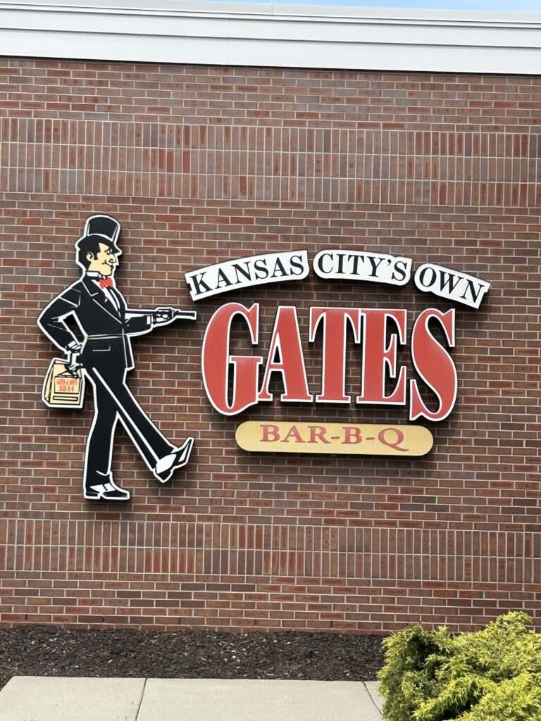 The struttin’ man logo of Gates Bar-B-Q, a mainstay in Kansas City all five locations . The iconic Kansas City's Own Gates Bar-B-Q sign and Struttin' Man emblem mounted on a red brick building.