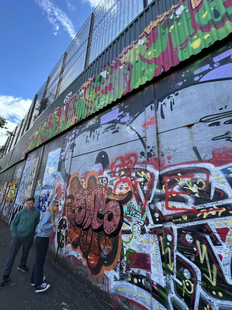 The Peace Wall in Belfast, Northern Ireland A towering concrete dividing Peace Wall layered with colorful street art, graffiti, and messages of hope during a Belfast walking tour.