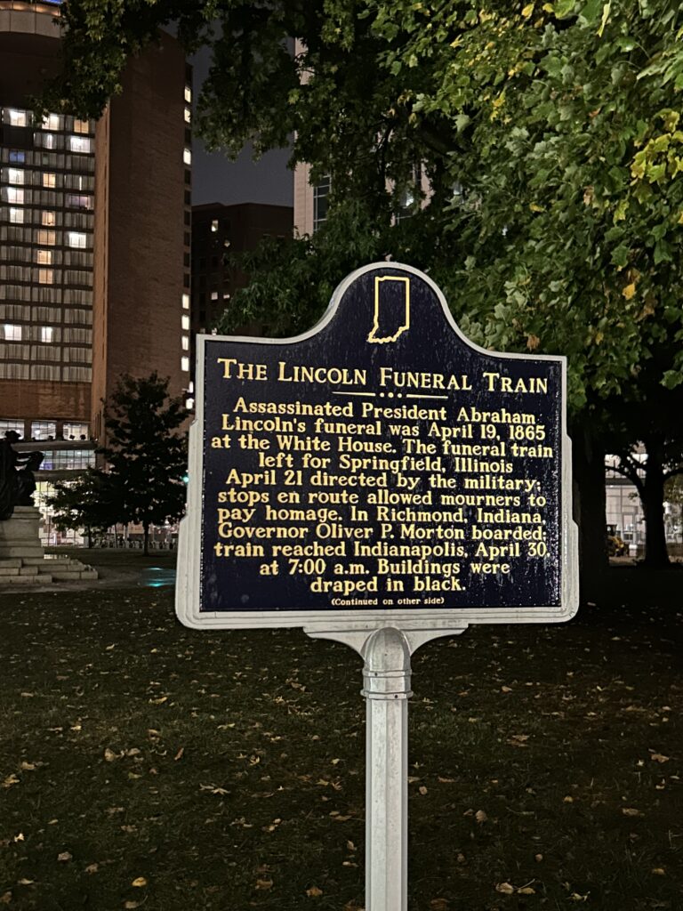 On the grounds of the Indiana Statehouse is the monument commemorating the funeral train of Abraham Lincoln. After being killed at Ford's Theatre in Washington, Lincoln's body was transported back to his home in Springfield, Illinois with many stops along the way. One of those stops was at the statehouse in Indianapolis. A close-up of a dark blue and gold Indiana historical marker detailing a spooky local legend during a haunted Indy tour.