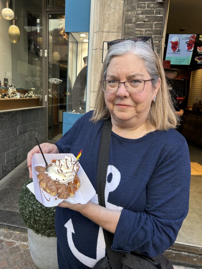 The perfect way to start a morning in Belgium, with a waffle covered in chocolate and whipped cream from Chez Albert near the Markt Square in Bruges. A close-up of a delicious, freshly made street-food waffle being held during a Bruges day trip.