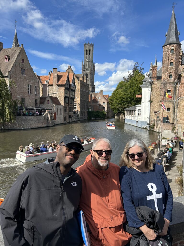 Bruges is a beautiful city, and the best place to capture that beauty is at Rosary Quay. The spot where you go for a canal boat tour is also the perfect place to capture a photo of the canal and the historic buildings. A small group of travelers gathering along the historic stone canal stone walls during a Bruges day trip.