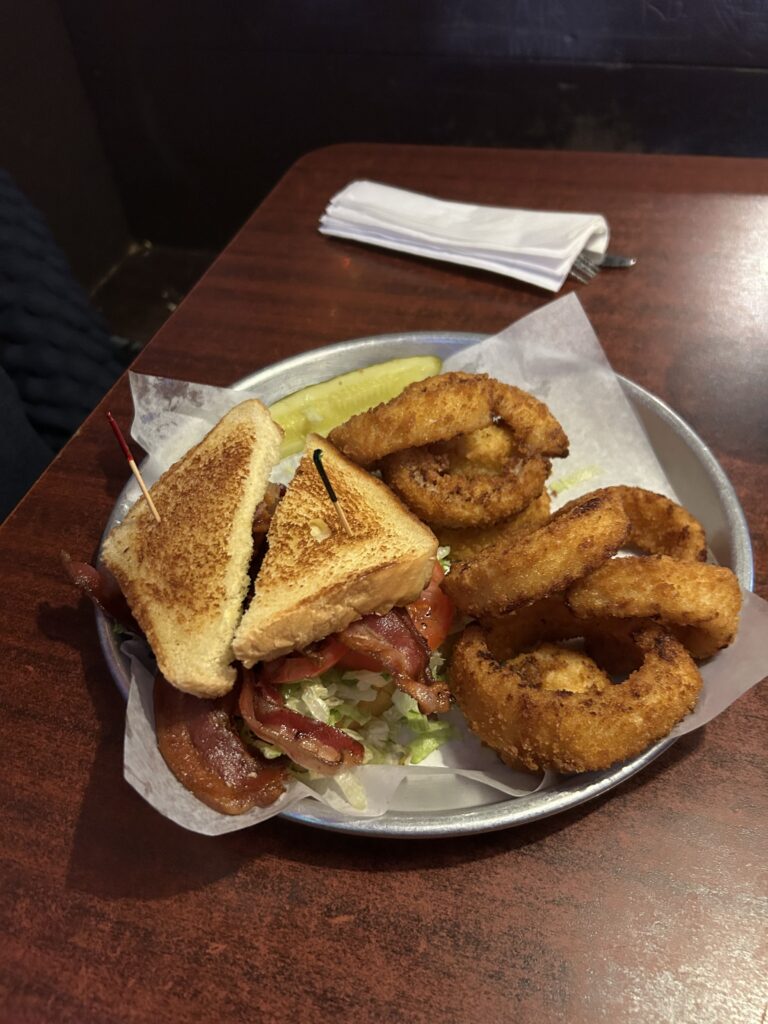 The Thurman Cafe is more than just burgers, including a fantastic turkey club sandwich and world-class onion rings. A massive BLT sandwich bursting with crispy bacon next to a basket of thick-cut golden onion rings at the Thurman Cafe Columbus Ohio.