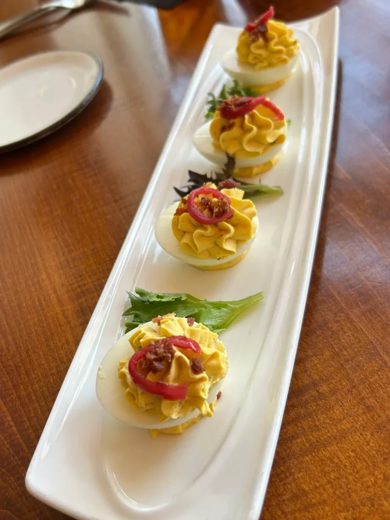 Golden Lamb has a strong offering of appetizers to try. Our selection was the very traditional deviled eggs. A close-up of a gourmet deviled eggs appetizer served on a white rectangular plate at The Golden Lamb restaurant in Ohio.