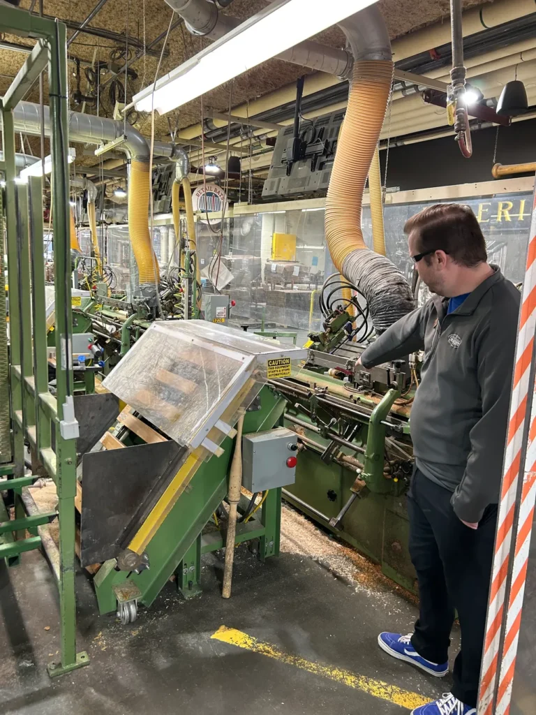 A man observing the automated lathe process as a wooden billet is shaped into a baseball bat during the Louisville Slugger factory tour.