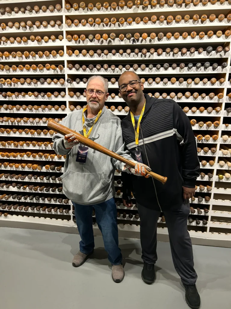 Two men wearing protective gloves while holding a historic Jackie Robinson model game-used baseball bat inside the Bat Vault at the Louisville Slugger Museum.