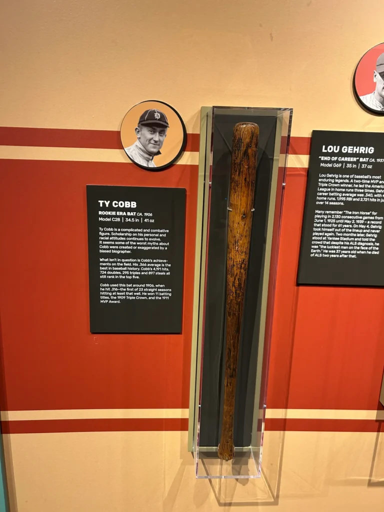 A historic Ty Cobb game-used baseball bat on display next to a biography panel inside the Louisville Slugger Museum & Factory.