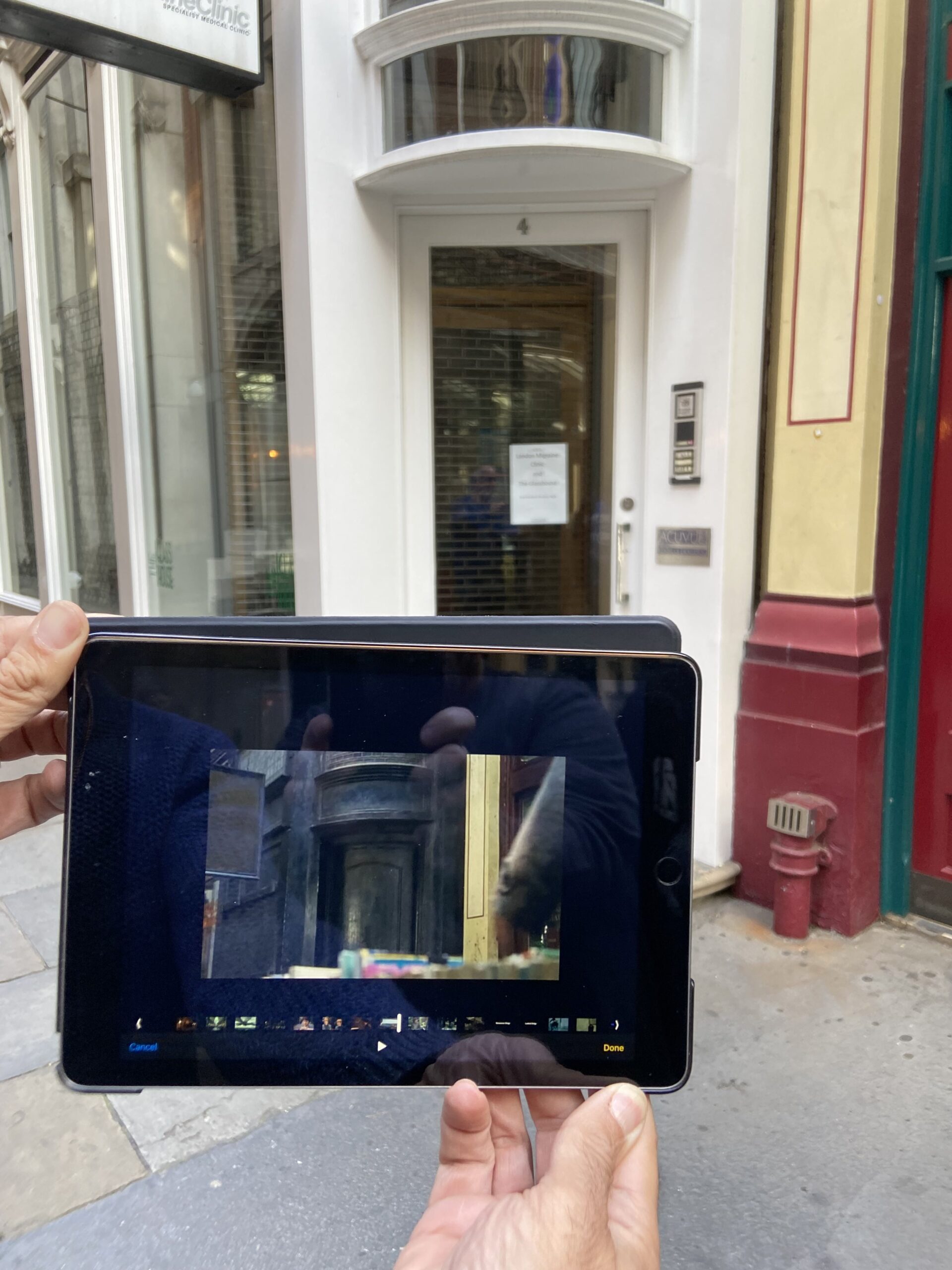 A tour guide holding a tablet showing a movie scene next to the real Leaky Cauldron entrance doorway in Leadenhall Market on a Harry Potter London taxi tour.