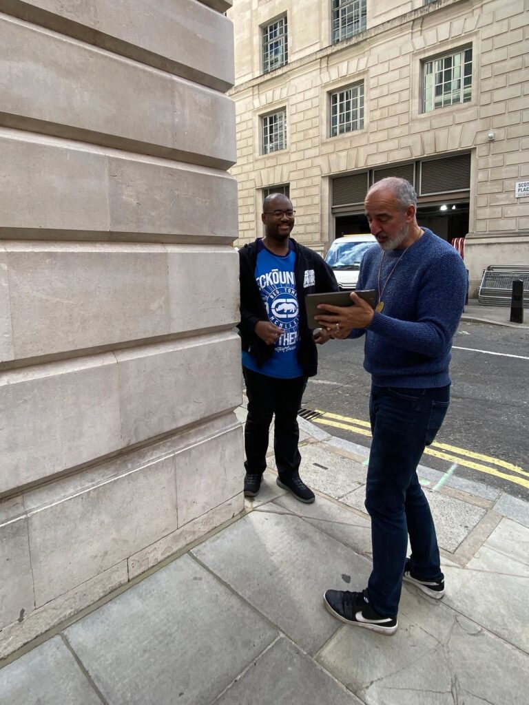 A tour guide showing a tablet to a visitor outside the Scotland Place corner in London, a filming location for the Ministry of Magic entrance on a Harry Potter London black taxi tour.